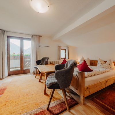 Helles Schlafzimmer der Ferienwohnung Hochjoch, Blick von Eingang auf Doppelbett, Stühle im Fußbereich und auf Sofa neben Balkontü