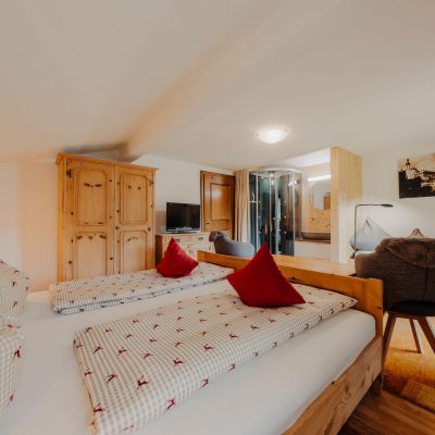 Helles Schlafzimmer der Ferienwohnung Hochjoch, Ausblick Doppelbett auf hellen Holzschrank und modernen Duschbereich mit Glasdusche