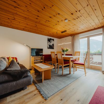 Helle Wohnküche der Ferienwohnung Mittagspitze im Haus Wilma, im gemütlichen, natürlichen Stil mit Holzdecke mit Blick auf rote Sitzecke und gemütliches graues Sofa.