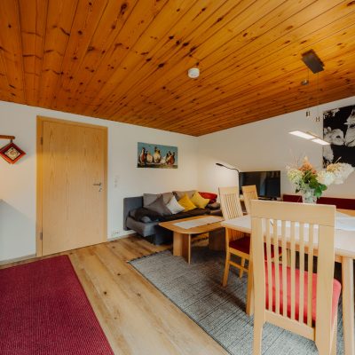 Helle Wohnküche der Ferienwohnung Mittagspitze mit Blick vom Balkon in Richtung Tür. Moderne Küchenzeile zur linken, Essbereich zur Rechten und graues Sofa rechts hinten.