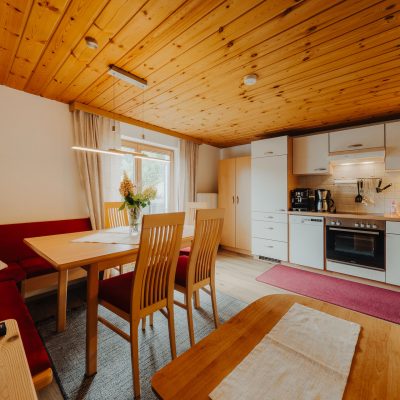 Helle Wohnküche der Ferienwohnung Mittagspitze im Haus Wilma, im gemütlichen, natürlichen Stil mit Holzdecke, roter Sitzecke und moderner Küchenzeile.