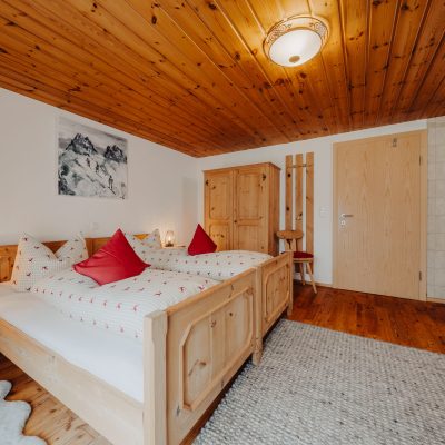 erstes Schlafzimmer der Ferienwohnung Mittagspitze mit Holzdecke im Haus Wilma, helles rustikales Doppelbett mit hellen Holzmöbeln
